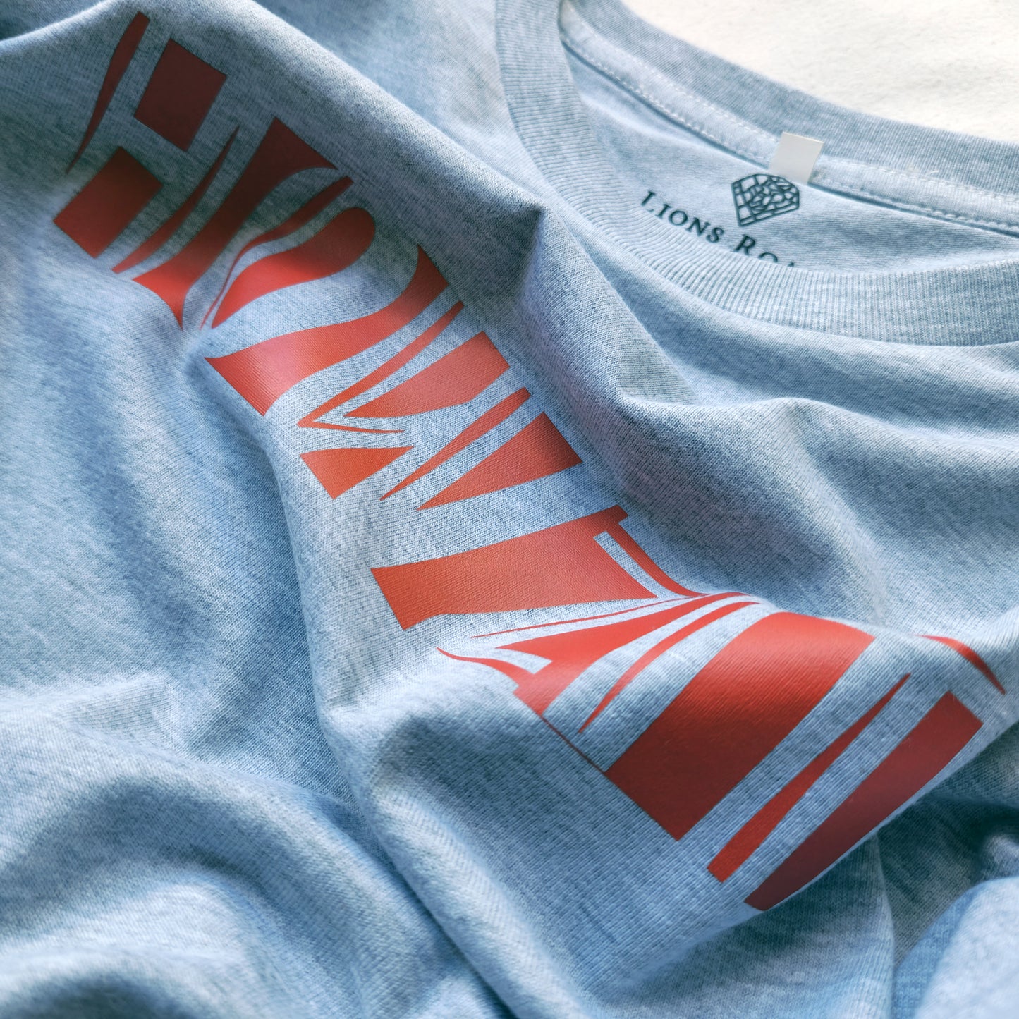 A Grey t-shirt with the phrase "Howzit" printed in Red.