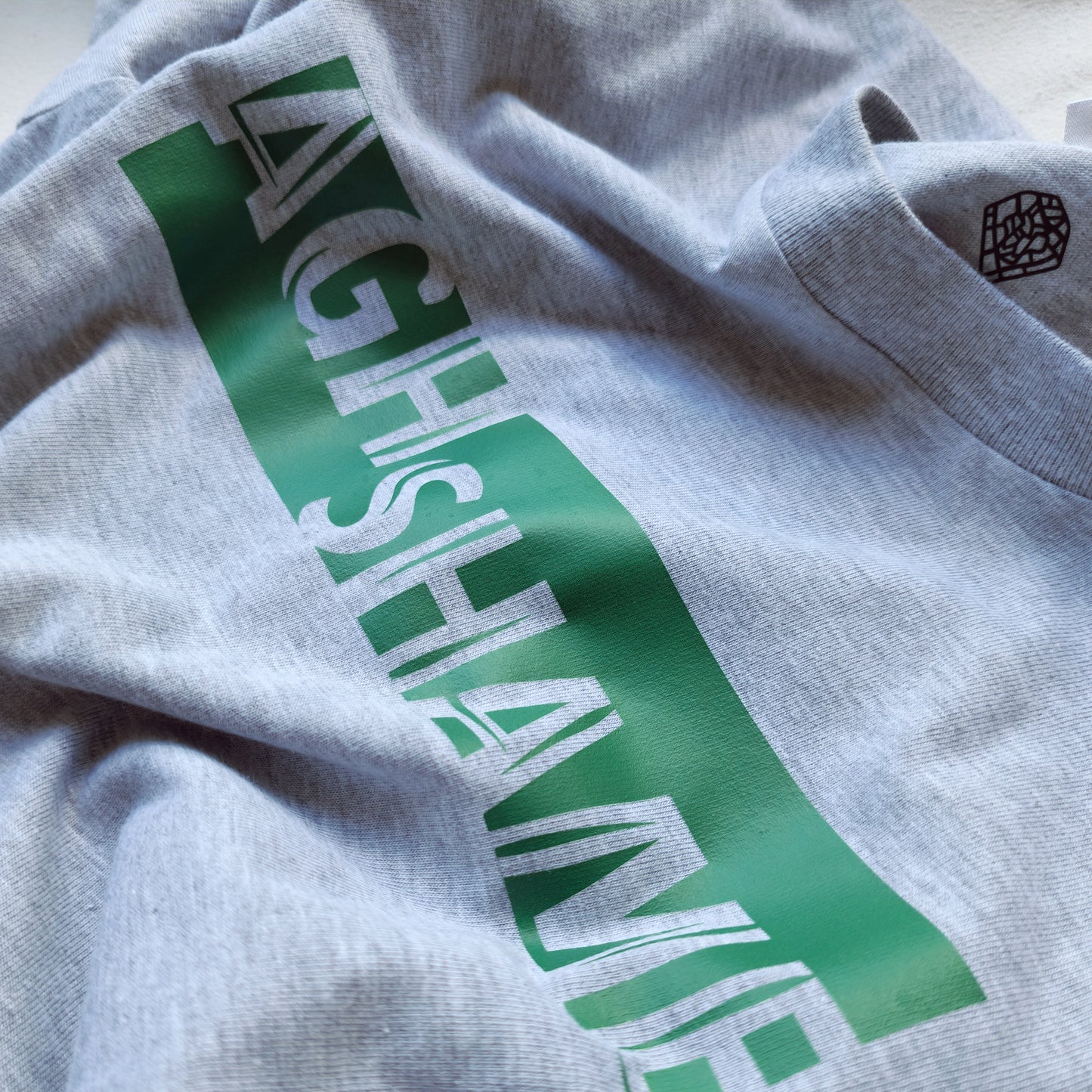 A Grey t-shirt with the phrase "Agh Shame" printed in Green.
