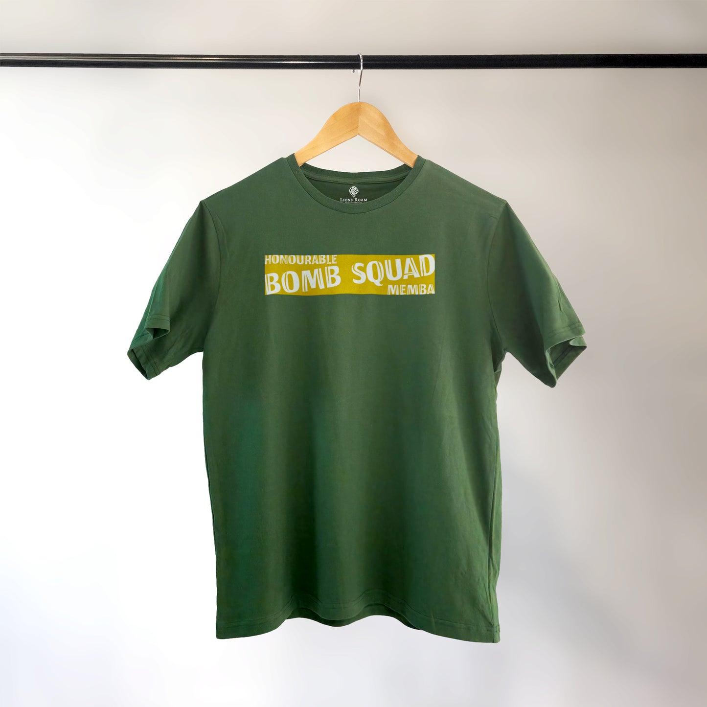 Green Lions Roam t-shirt with the phrase 'Honourable Bomb Squad Memba' printed on the front, displayed on a wooden hanger against a neutral background. The shirt hangs neatly, showcasing its bold, statement design.