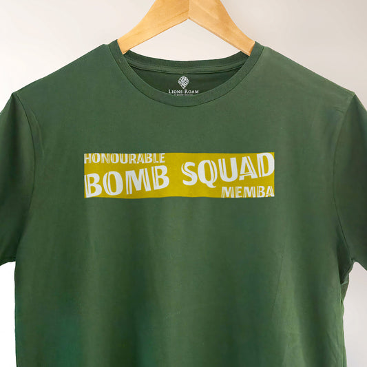 Green Lions Roam t-shirt with the phrase 'Honourable Bomb Squad Memba' printed on the front, displayed on a wooden hanger against a neutral background. The shirt hangs neatly, showcasing its bold, statement design.