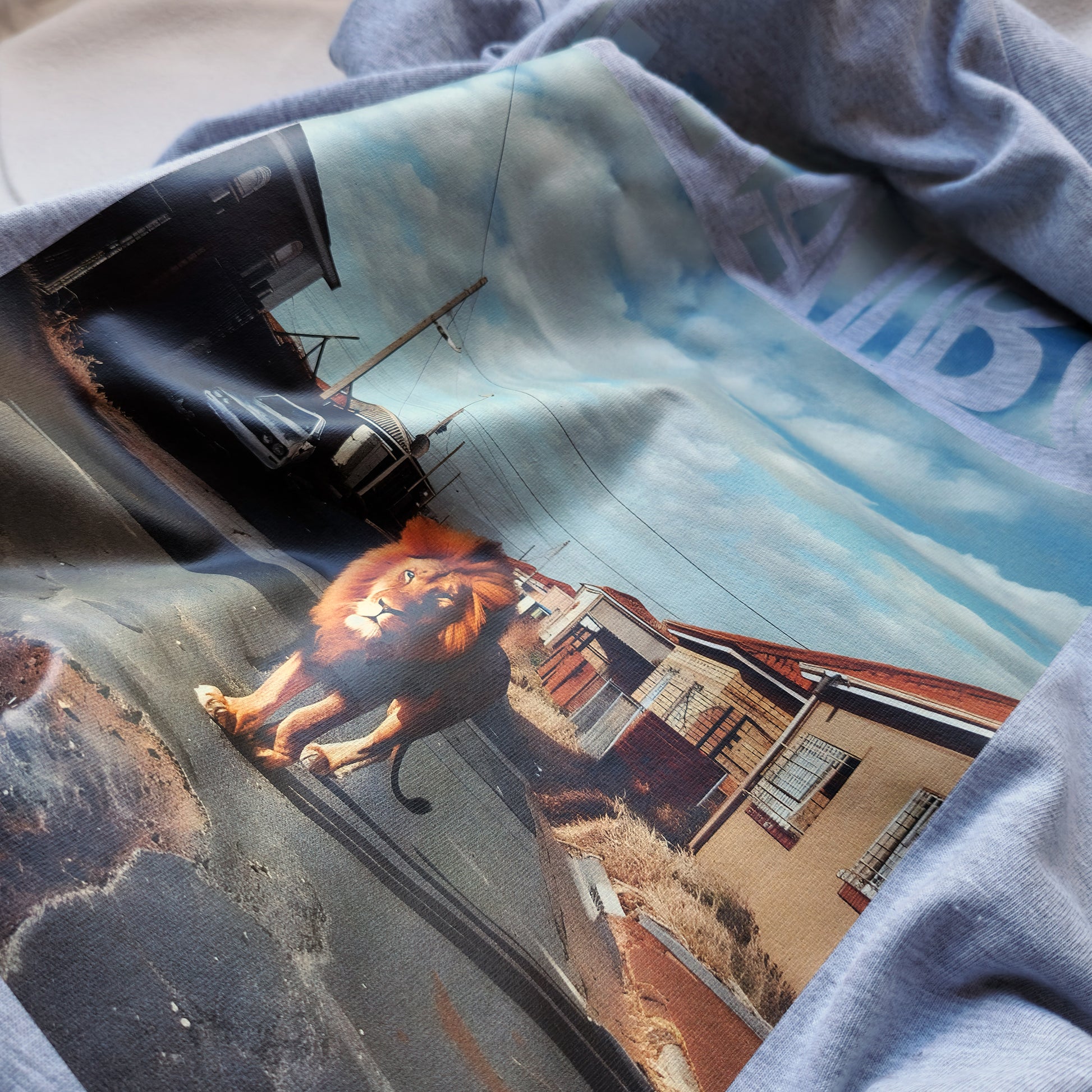 A Grey t-shirt with the phrase "Haaibo" printed in the sky, with a lion roaming the streets of africa.