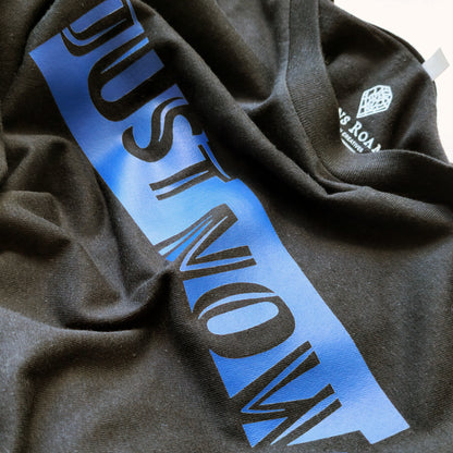 A black t-shirt with the phrase "Just Now" printed in Blue.