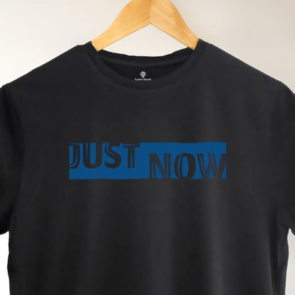 A black t-shirt with the phrase "Just Now" printed in Blue.