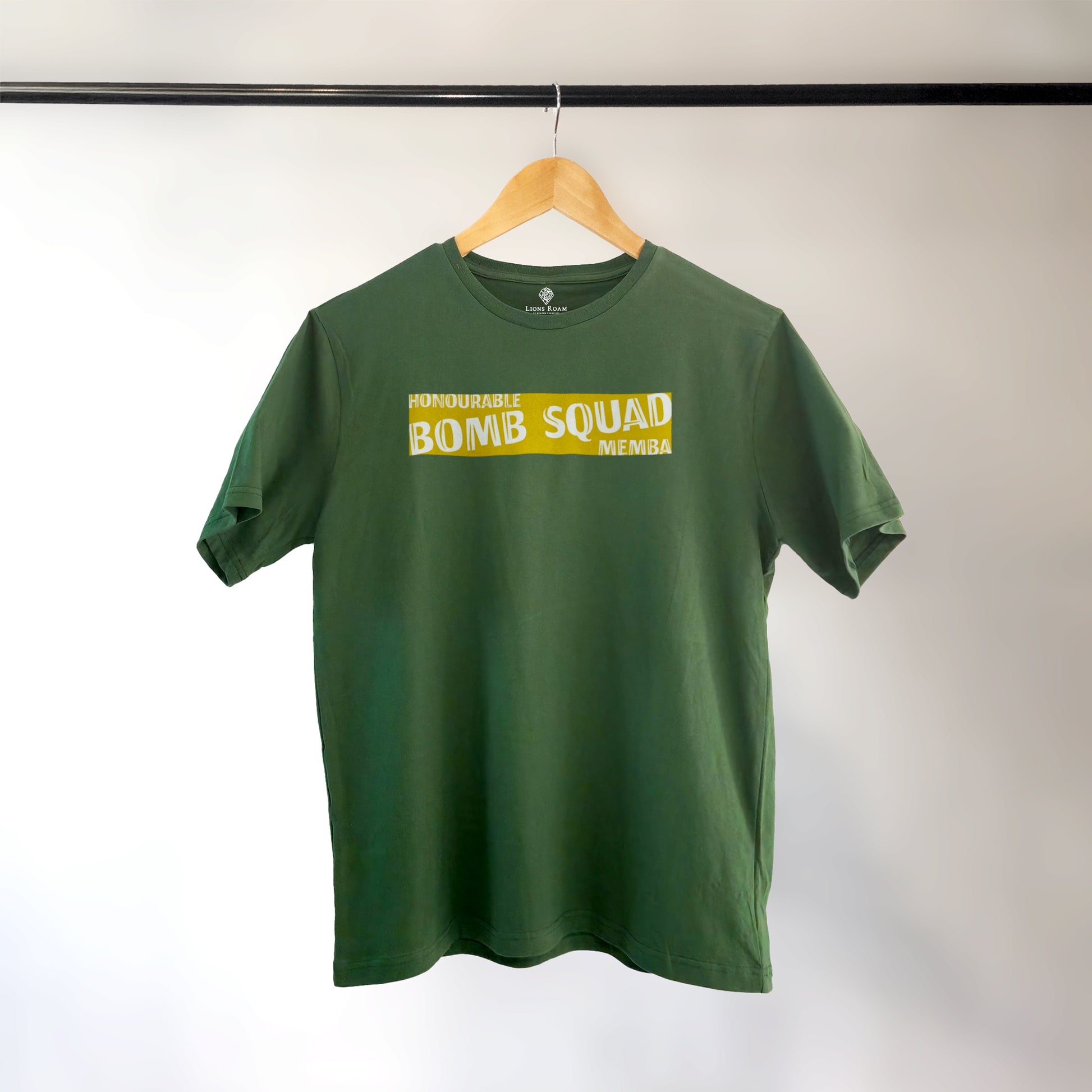 Green Lions Roam t-shirt with the phrase 'Honourable Bomb Squad Memba' printed on the front, displayed on a wooden hanger against a neutral background. The shirt hangs neatly, showcasing its bold, statement design.