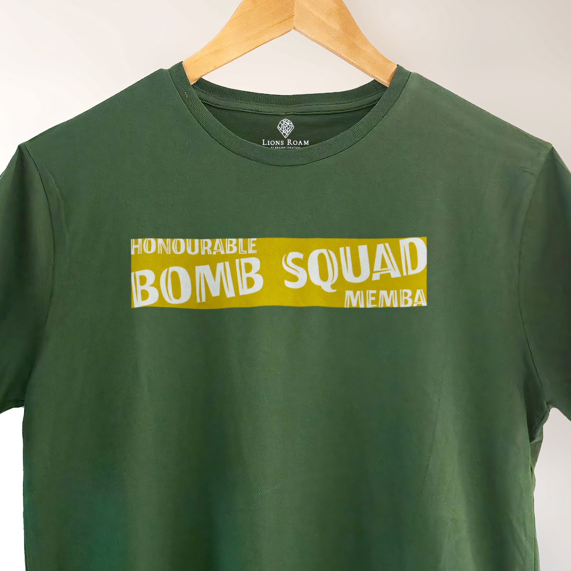 Green Lions Roam t-shirt with the phrase 'Honourable Bomb Squad Memba' printed on the front, displayed on a wooden hanger against a neutral background. The shirt hangs neatly, showcasing its bold, statement design.