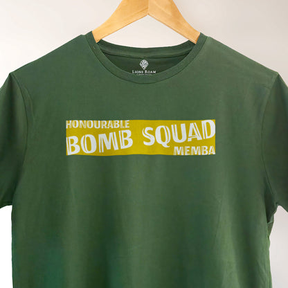 Green Lions Roam t-shirt with the phrase 'Honourable Bomb Squad Memba' printed on the front, displayed on a wooden hanger against a neutral background. The shirt hangs neatly, showcasing its bold, statement design.