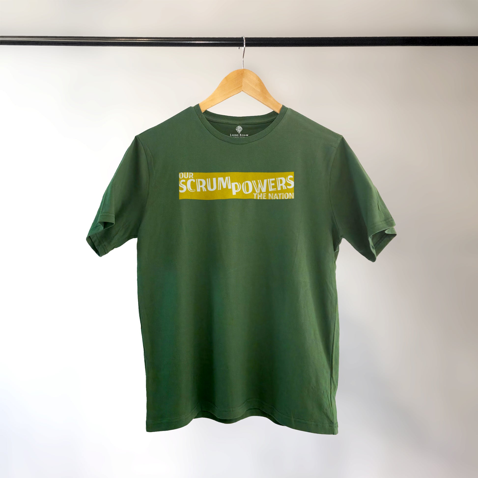 Green Lions Roam t-shirt with the phrase 'Our Scrum Powers the Nation' displayed on a hanger against a neutral background. The bold design makes a witty reference to South African resilience and rugby pride.