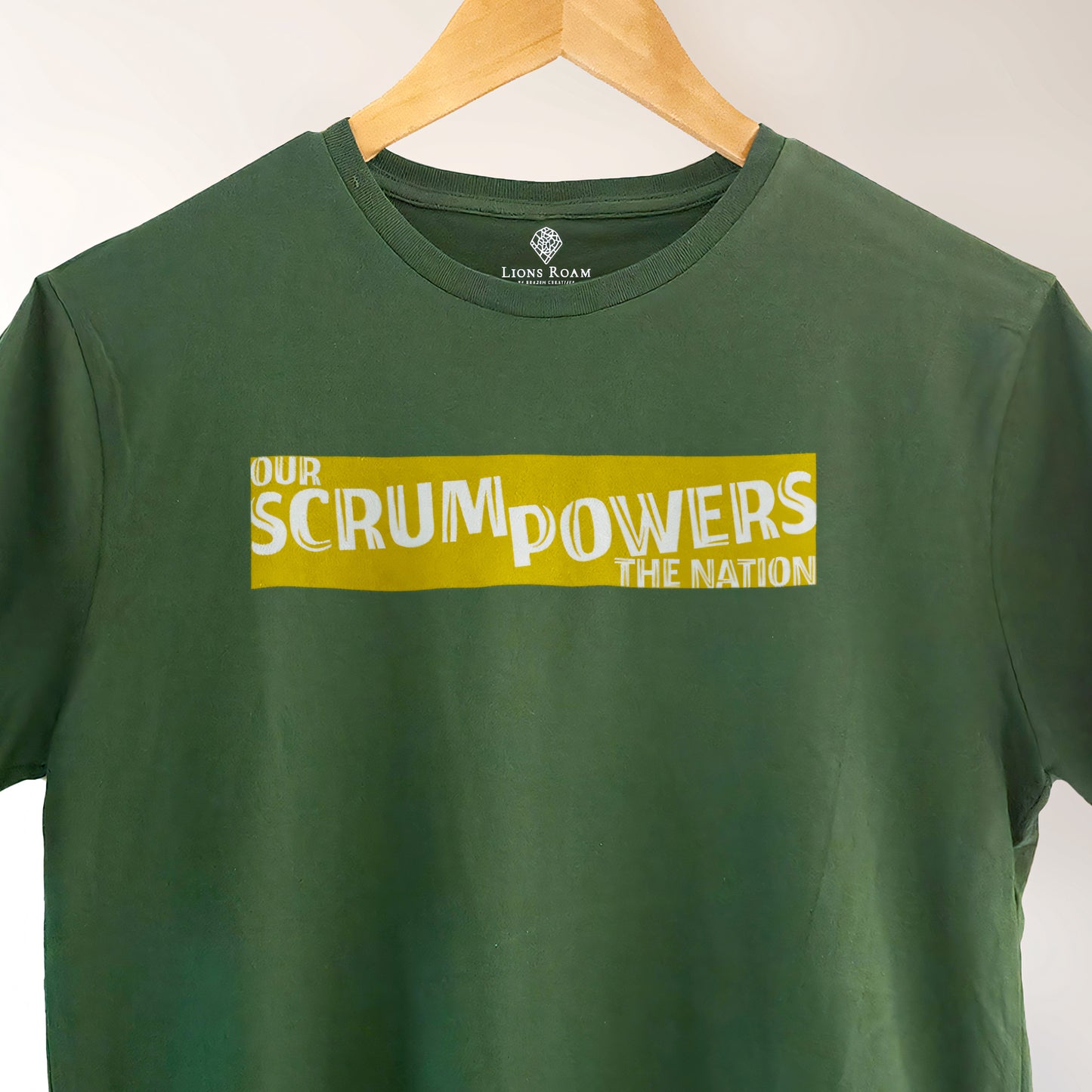 Green Lions Roam t-shirt with the phrase 'Our Scrum Powers the Nation' displayed on a hanger against a neutral background. The bold design makes a witty reference to South African resilience and rugby pride.